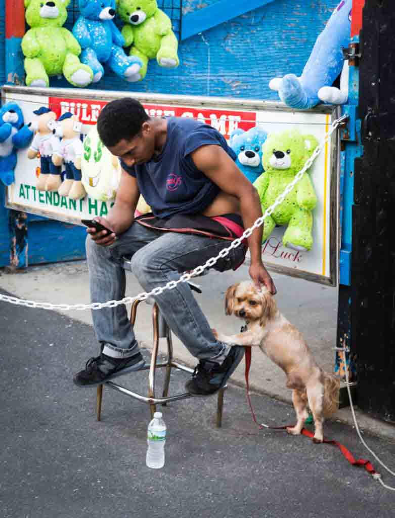 Coney Island street photography of a carnival worker petting dog