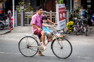 Father and child on bicycle for an article on the Cai Be Floating Markets