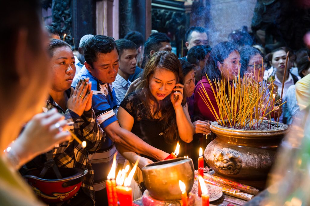 Woman lighting incense with cell phone at the Ba Thien Hau temple for article on Ho Chi Minh City street photos