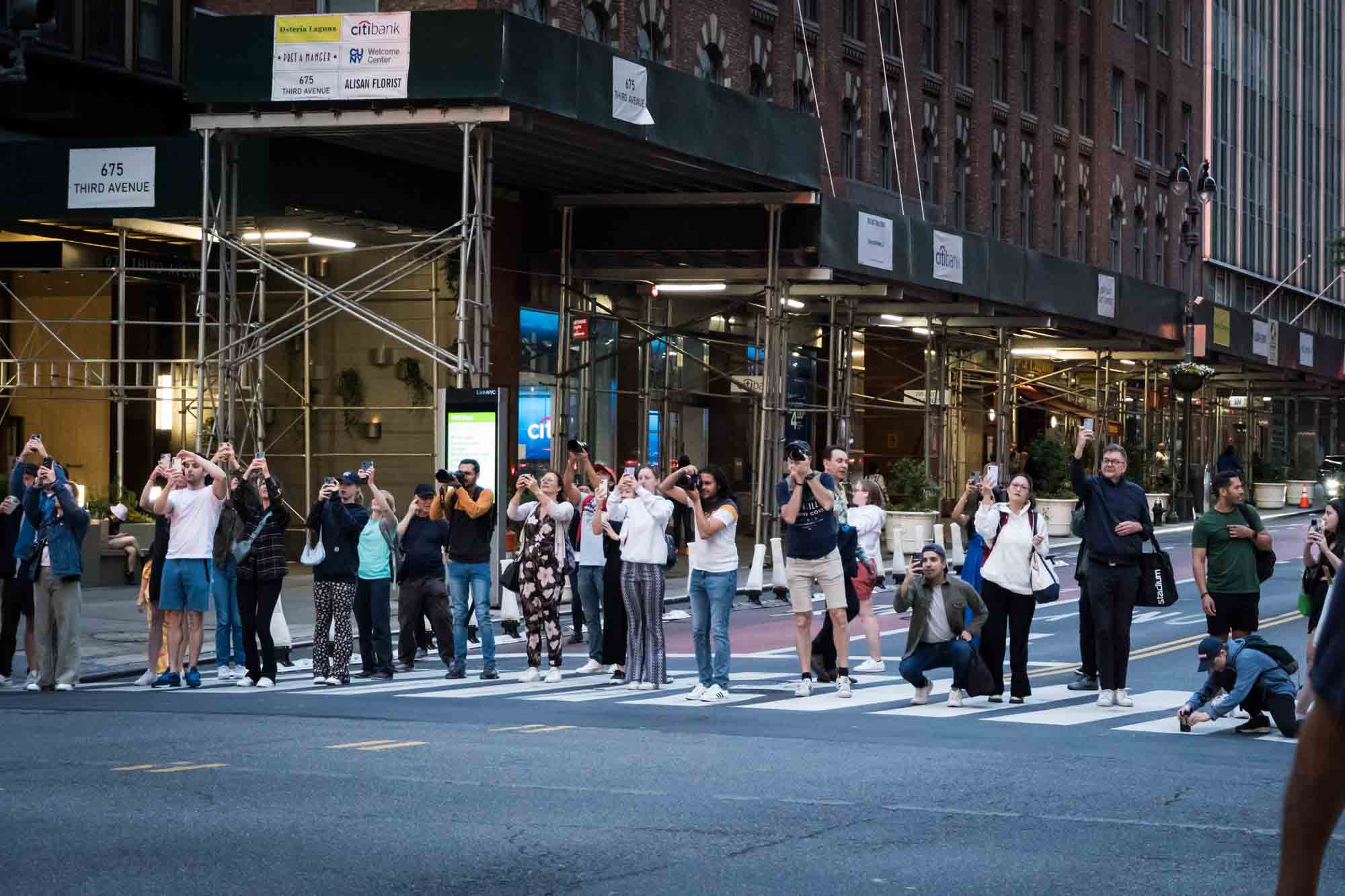 Tourists in a NYC crosswalk with cellphones in hand during Manhattanhenge