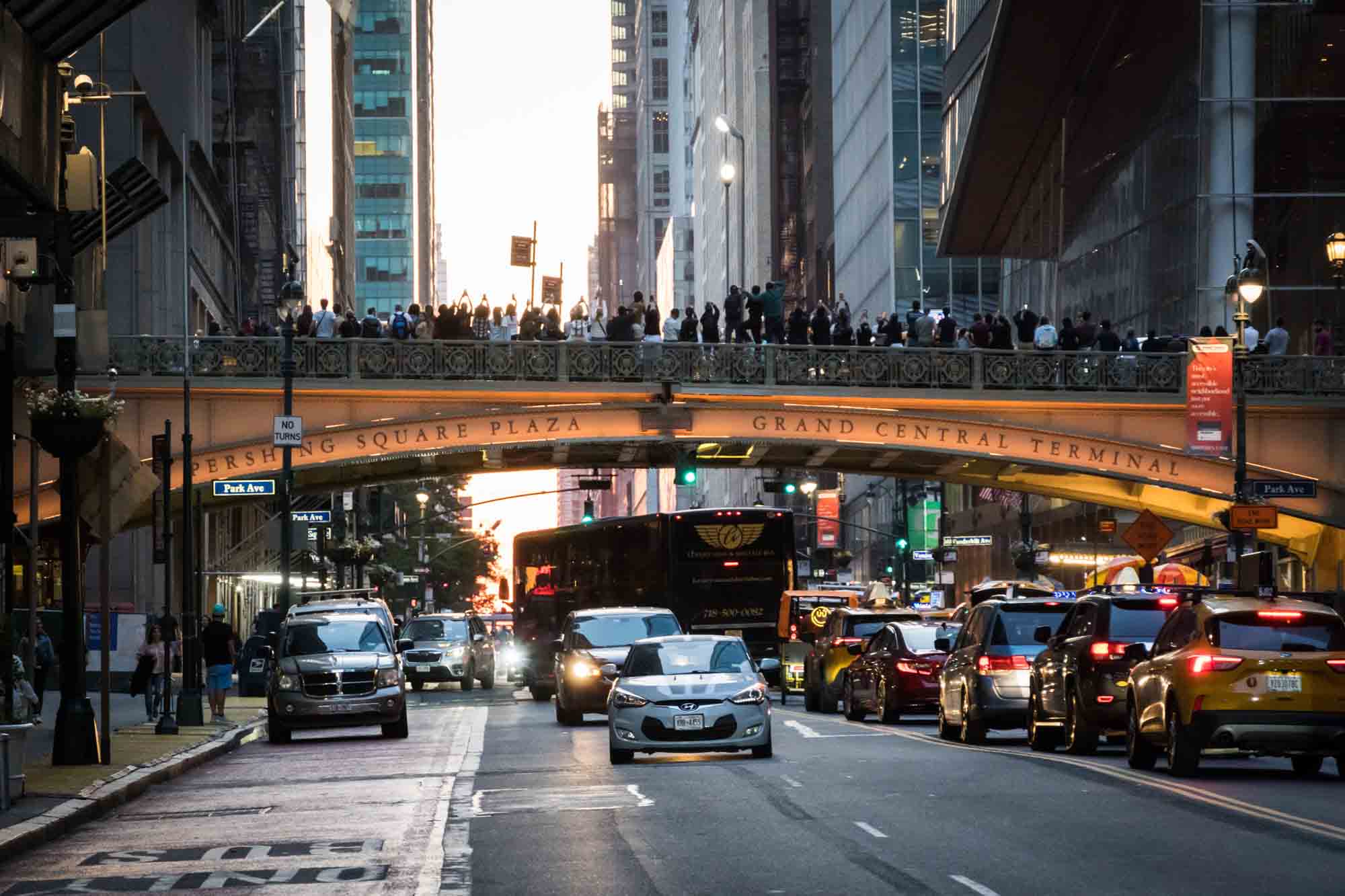 Tourists lined up on overpass watching Manhattanhenge with cars on street below