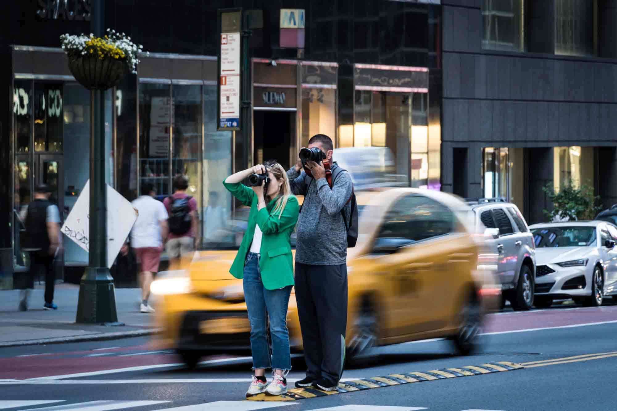 Two tourists with cameras to face in front of speeding taxi in middle of NYC street during Manhattanhenge