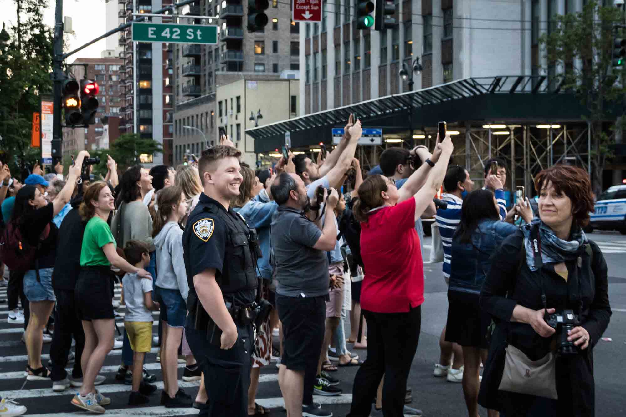 NYPD officer watching tourists in a NYC street with cellphones in hand during Manhattanhenge