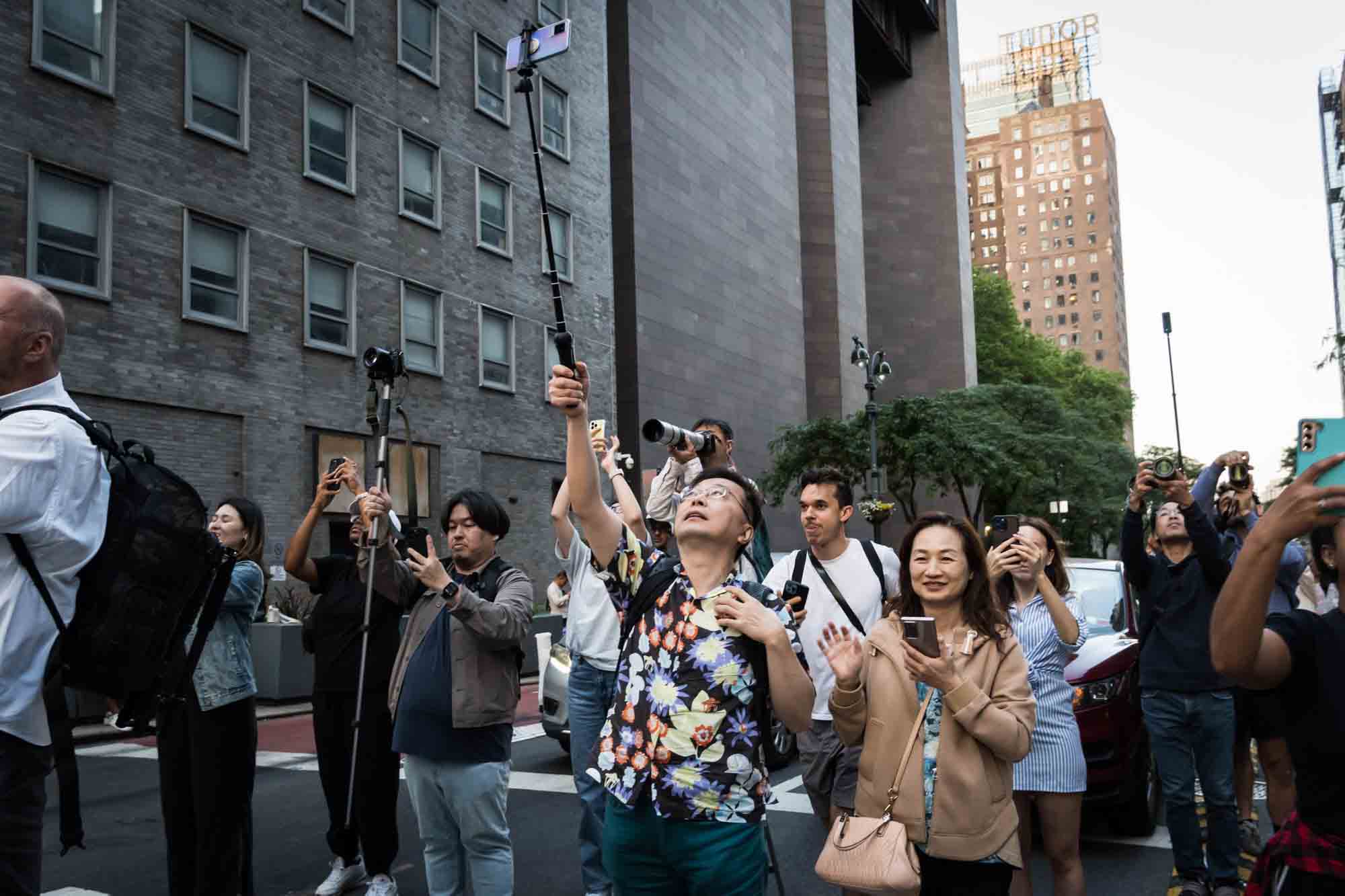 Asian man with cellphone on stick in a NYC street with cellphones in hand during Manhattanhenge