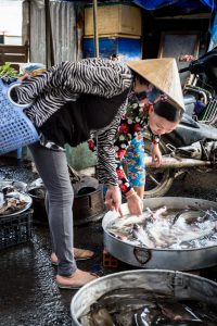 Two women choosing fish for an article on the Cai Be Floating Markets