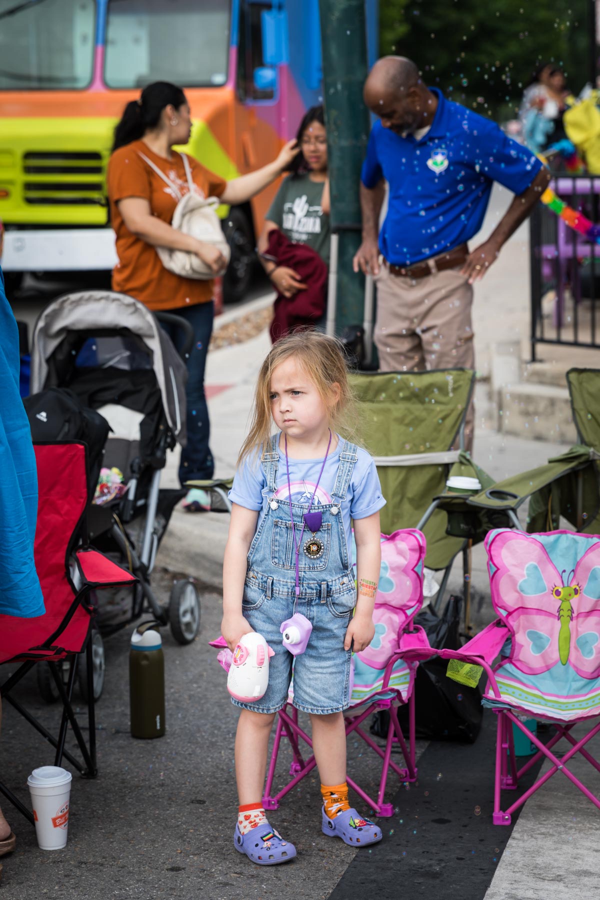 Little girl wearing blue shirt and overalls looking disappointed before parade for an article on the Fiesta photo tips