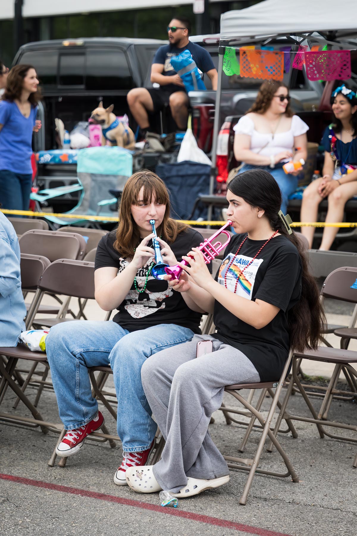 Two girls blowing toy horns and sitting in metal chairs for an article on the Fiesta photo tips