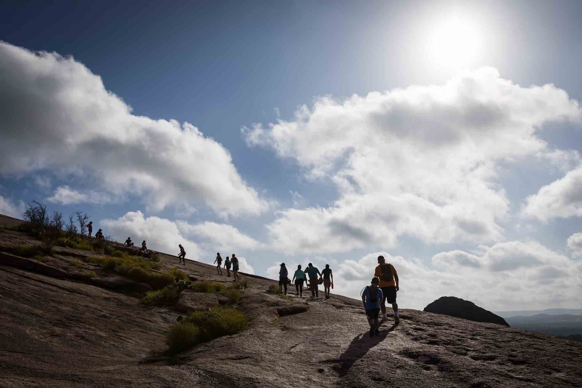 Silhouette of hikers climbing up mountain with clouds overhead for an article on Enchanted Rock hiking trips