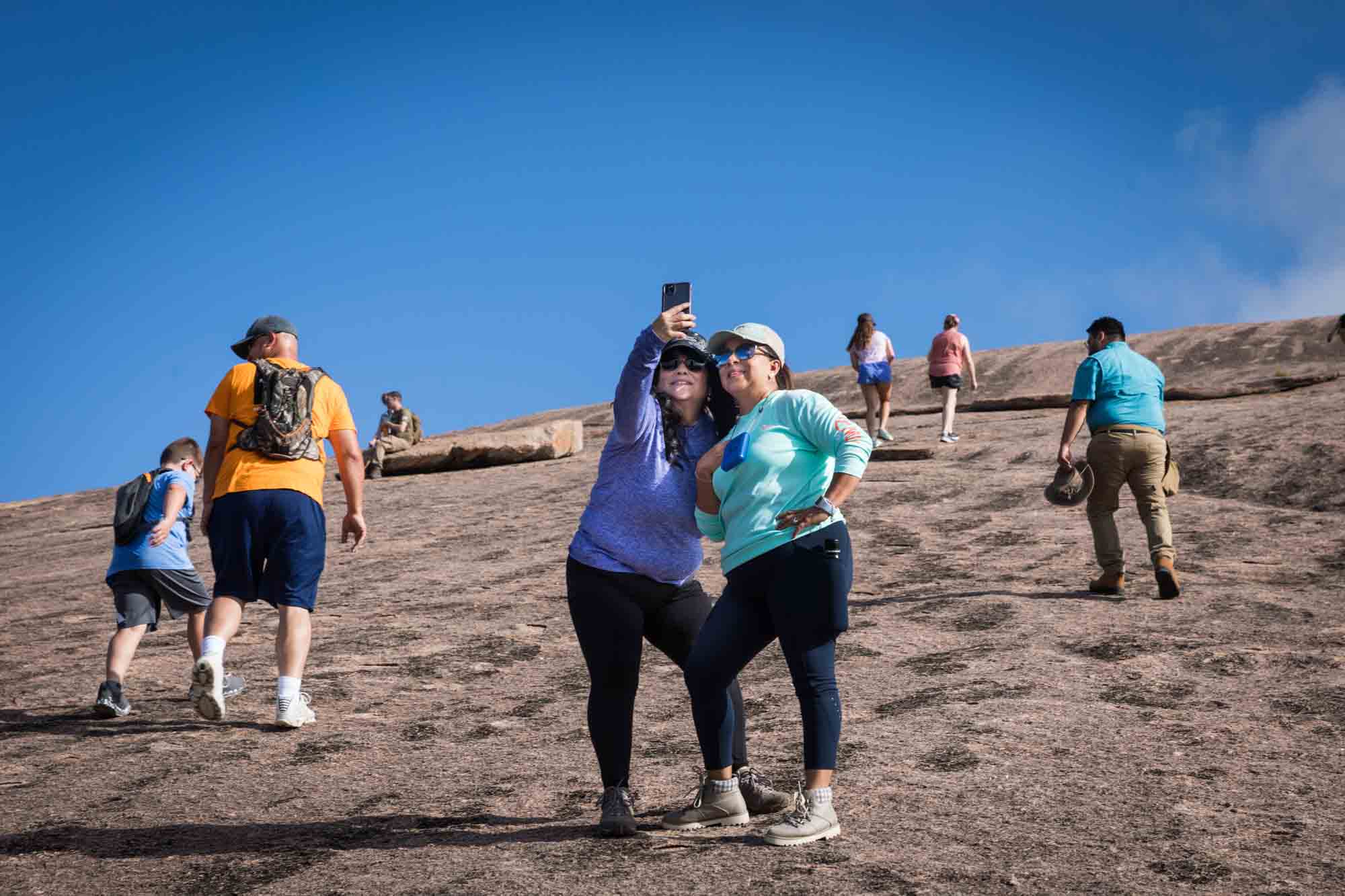 Two women taking a selfie surrounded by other hikers for an article on Enchanted Rock hiking trips