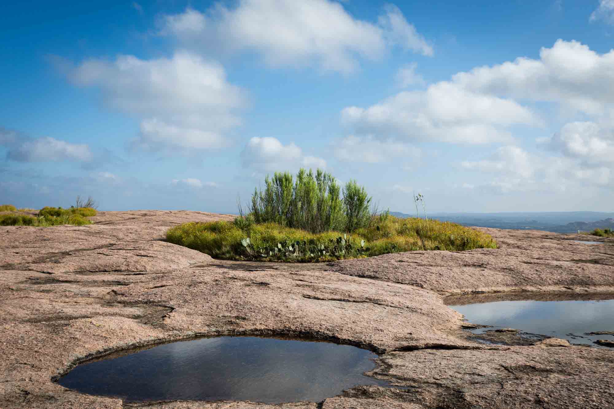 Patches of plants and pools of water with clouds overhead for an article on Enchanted Rock hiking trips