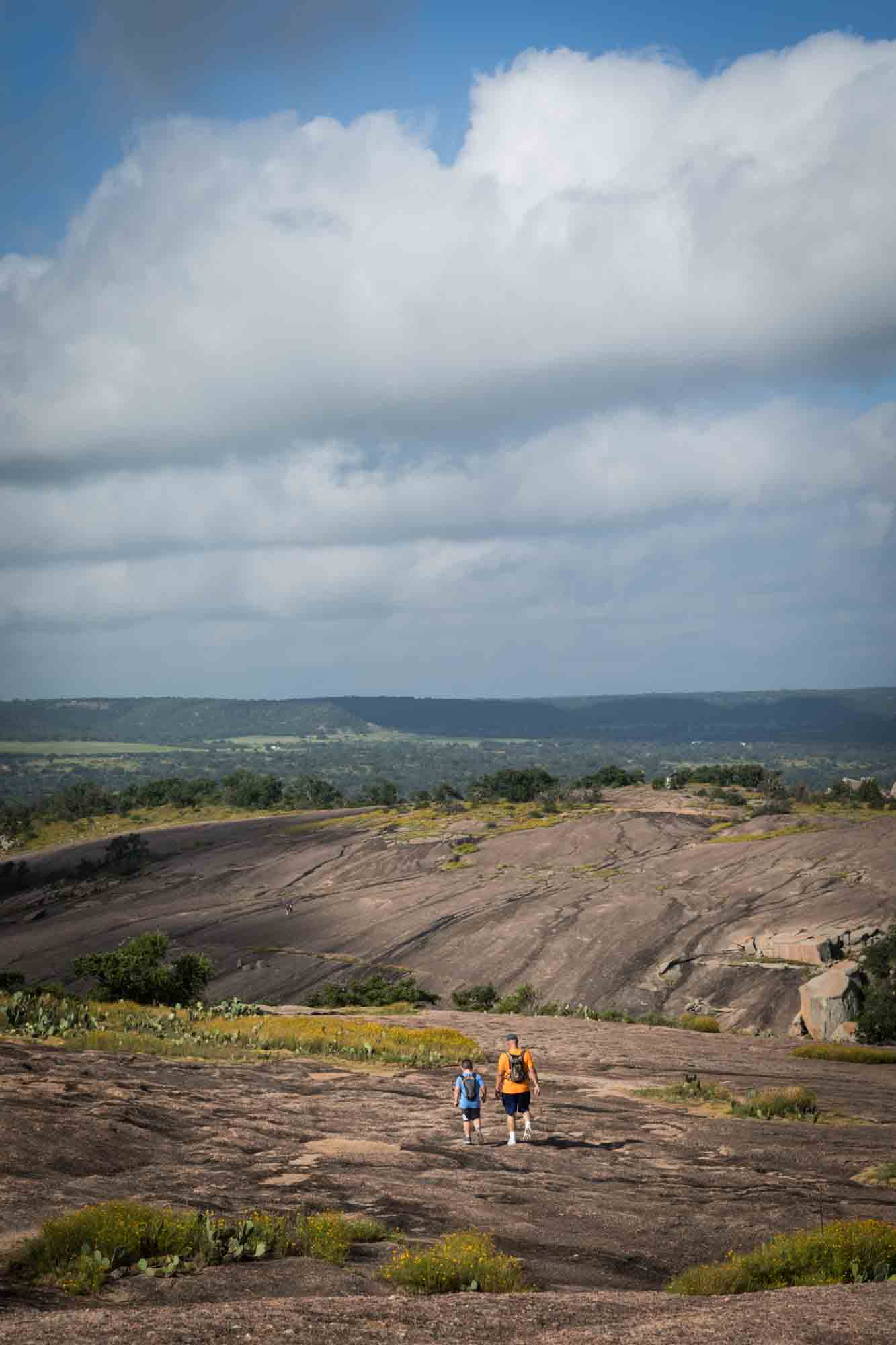 Father and son walking down mountain with clouds overhead for an article on Enchanted Rock hiking trips