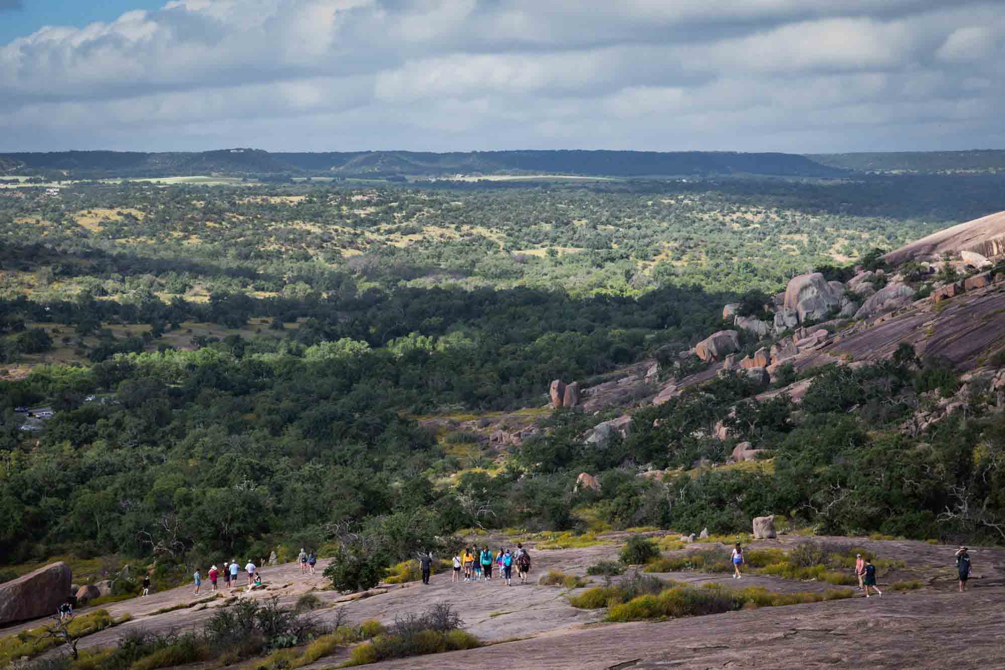 Hikers climbing up face of Enchanted Rock with view of trees in background for an article on Enchanted Rock hiking trips