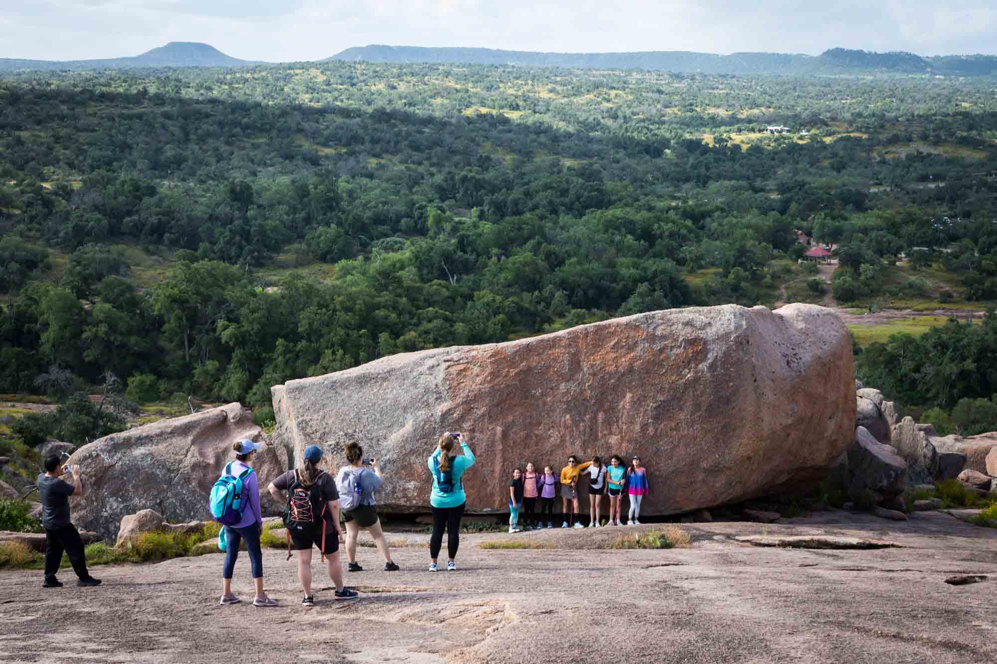 Hikers posed against large rock with view of trees in background for an article on Enchanted Rock hiking trips