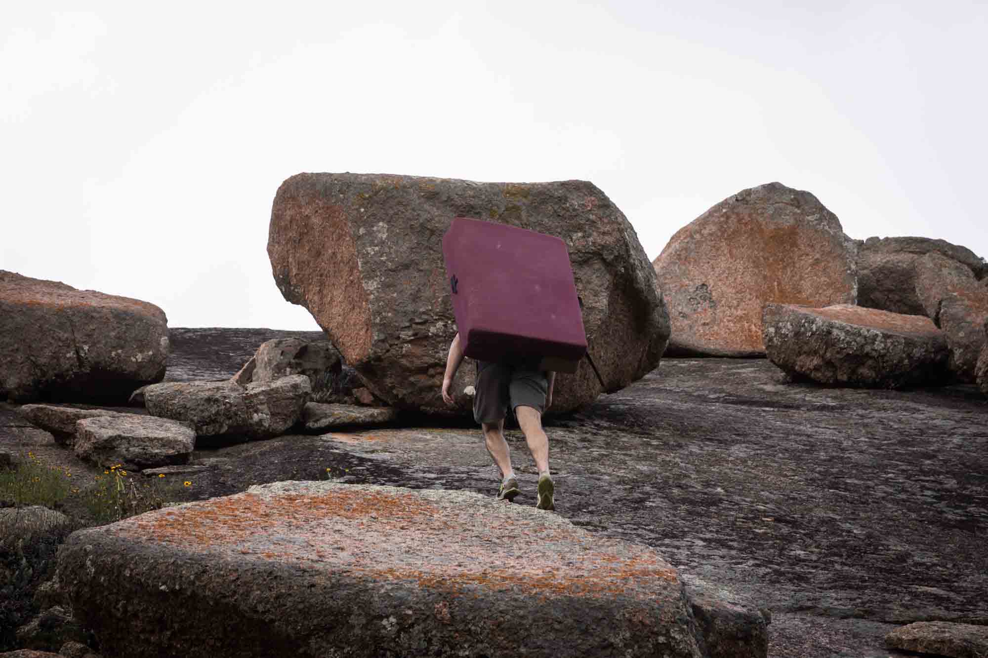 Hiker going up mountain with purple mattress strapped to his back for an article on Enchanted Rock hiking tips