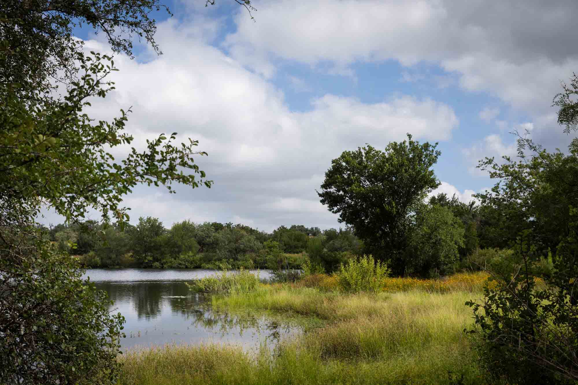 Moss Lake surrounded by trees, bushes, and clouds overhead for an article on Enchanted Rock hiking trips