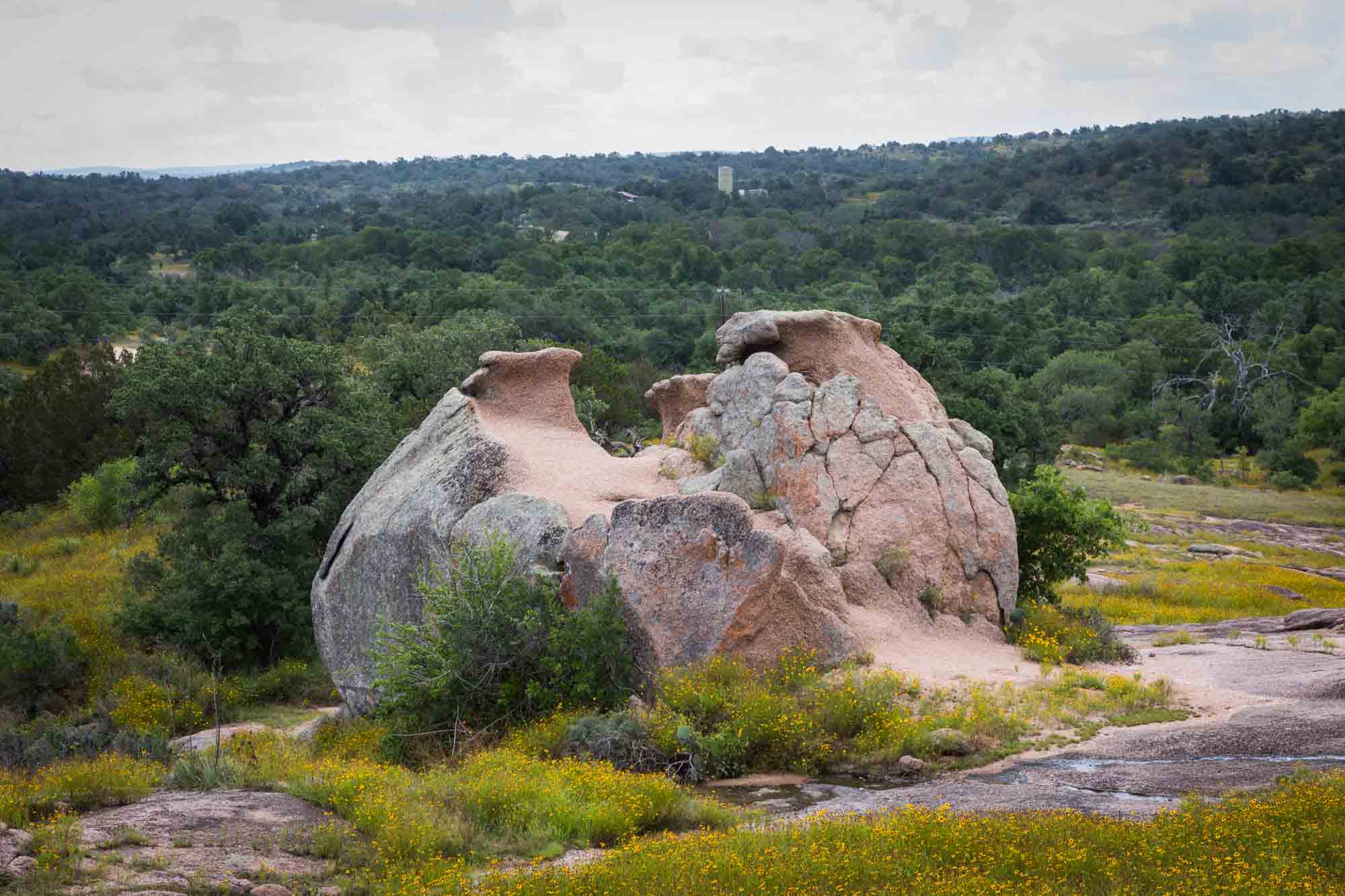 Weird egg-like rock formation with trees in the background for an article on Enchanted Rock hiking trips