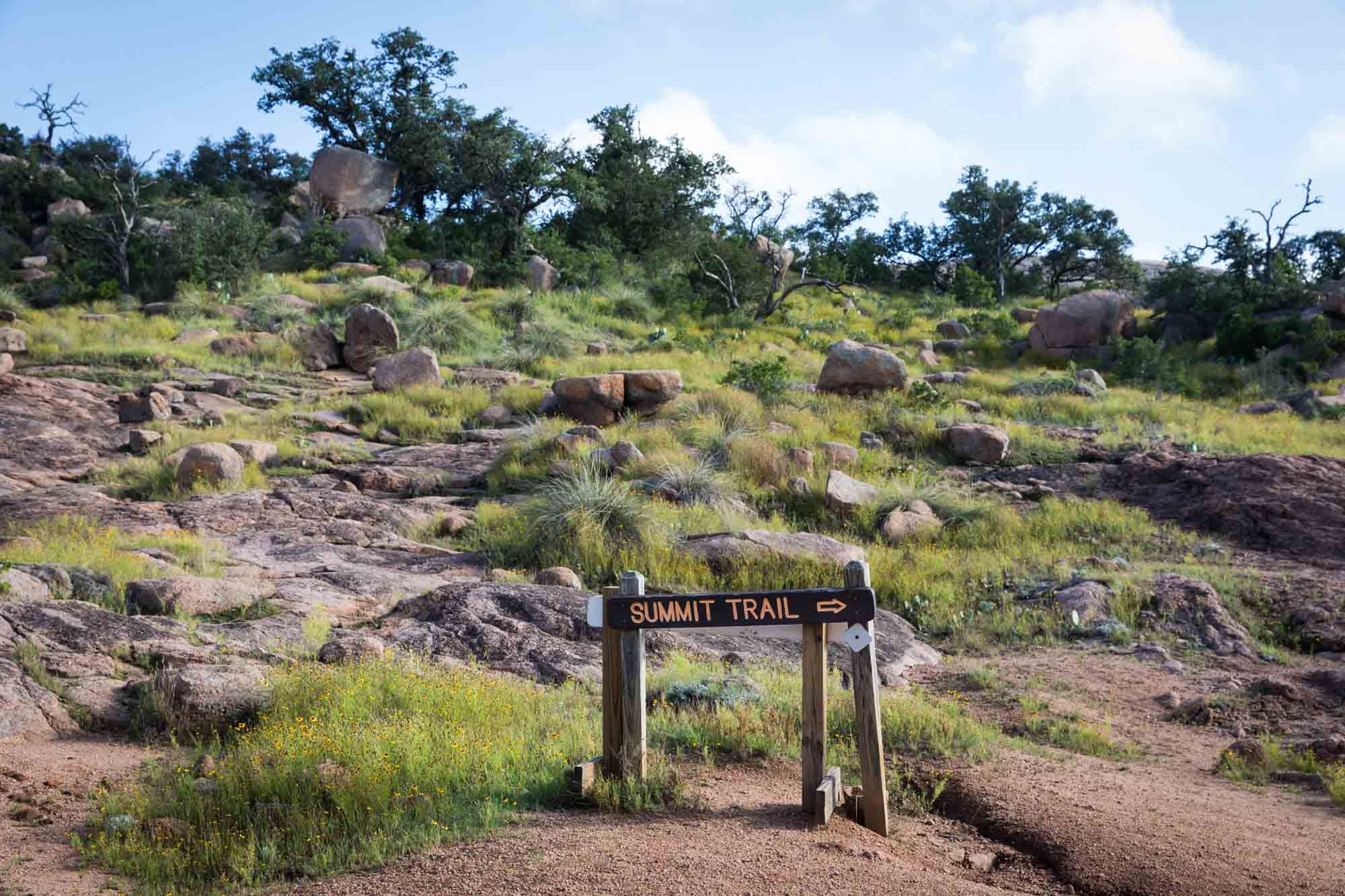 Summit trail sign in front of rocks and grass for an article on Enchanted Rock hiking trips