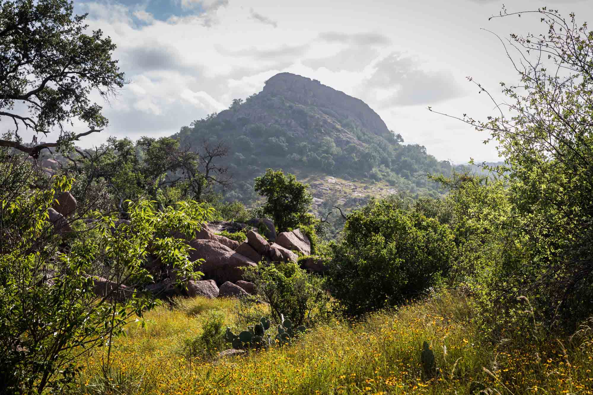 View of mountain in distance surrounded by trees and other rocks for an article on Enchanted Rock hiking trips