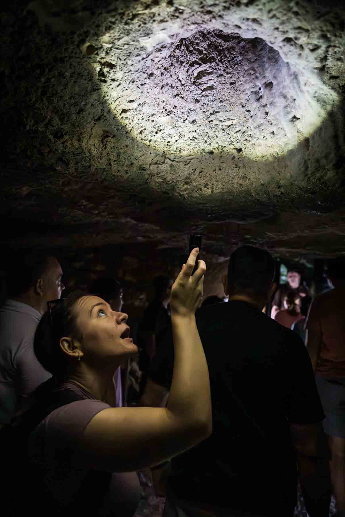 Woman shining flashlight into hole in Cascade Caverns for an article entitled, ‘Visiting Boerne, Texas: Everything You Need to Know’