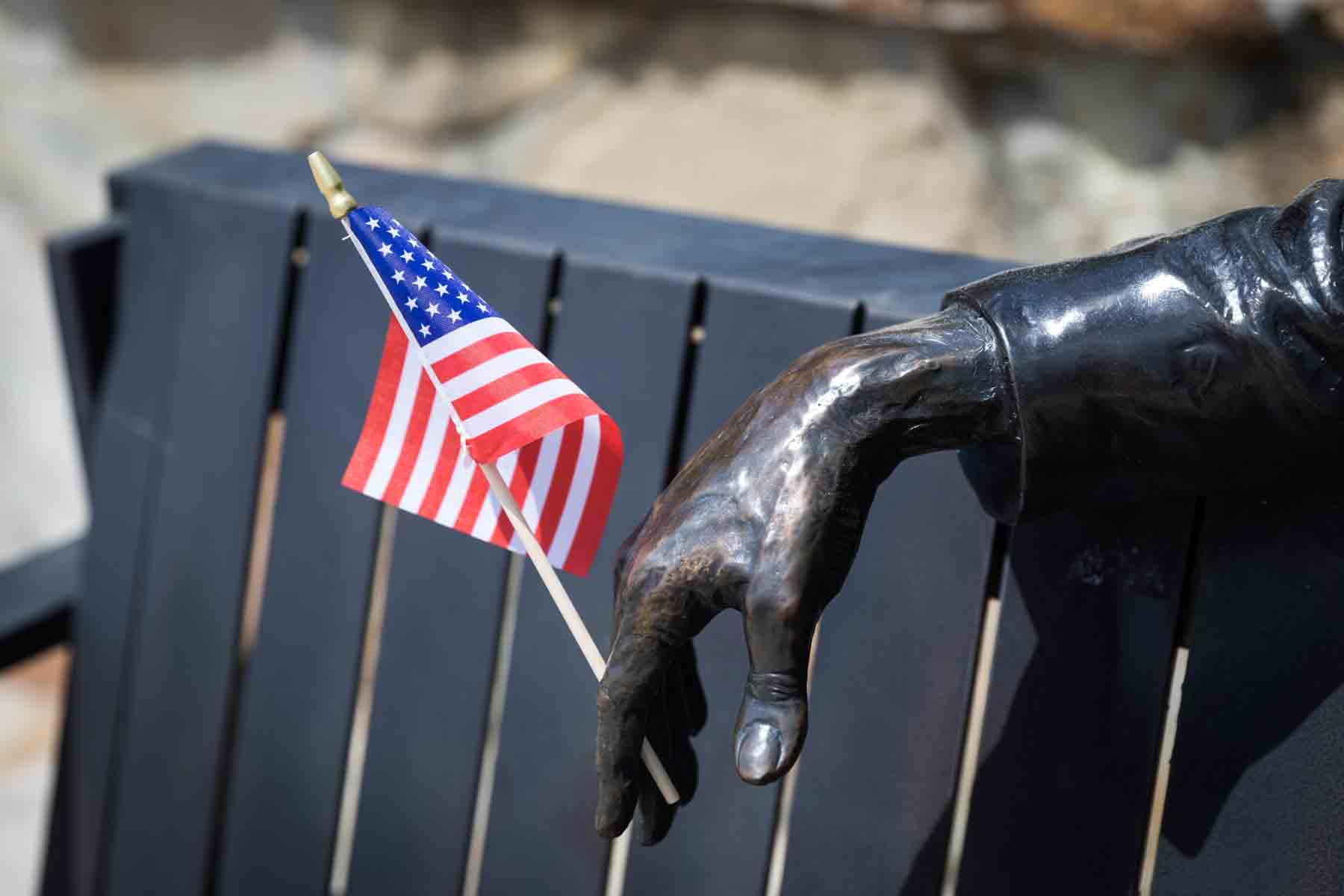 Hand of metal sculpture holding American flag on bench for an article entitled, ‘Visiting Boerne, Texas: Everything You Need to Know’