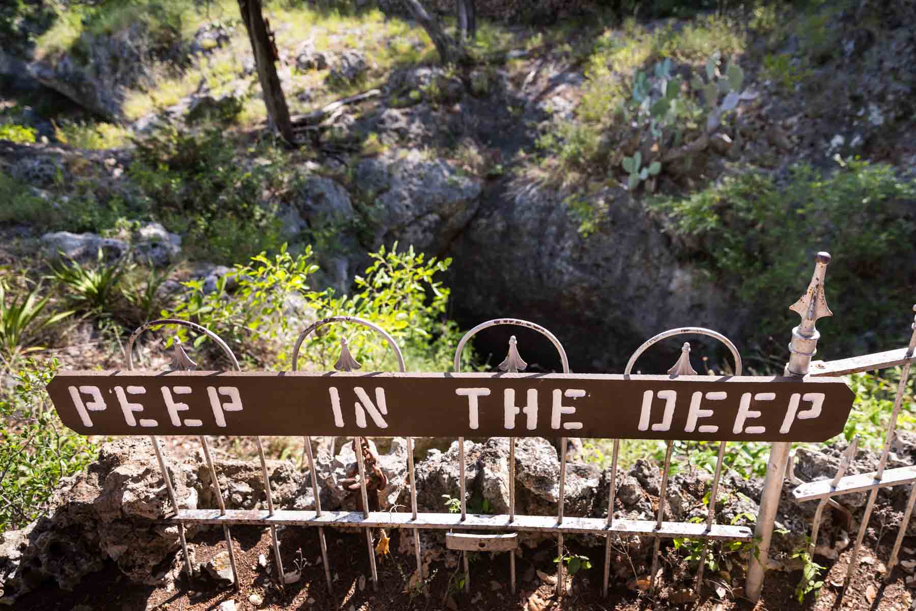 Metal fence sign for 'Peep in the Deep' in Cascade Caverns for an article entitled, ‘Visiting Boerne, Texas: Everything You Need to Know’