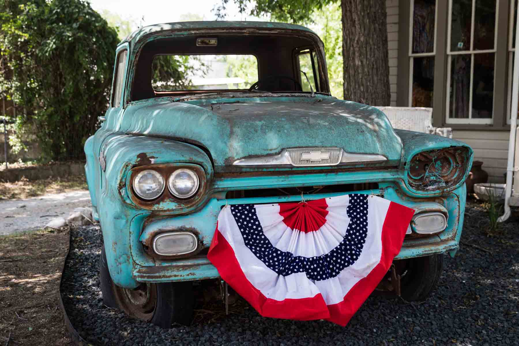 Old pickup truck colored teal with red, white, and blue flag on front of truck for an article entitled, ‘Visiting Boerne, Texas: Everything You Need to Know’