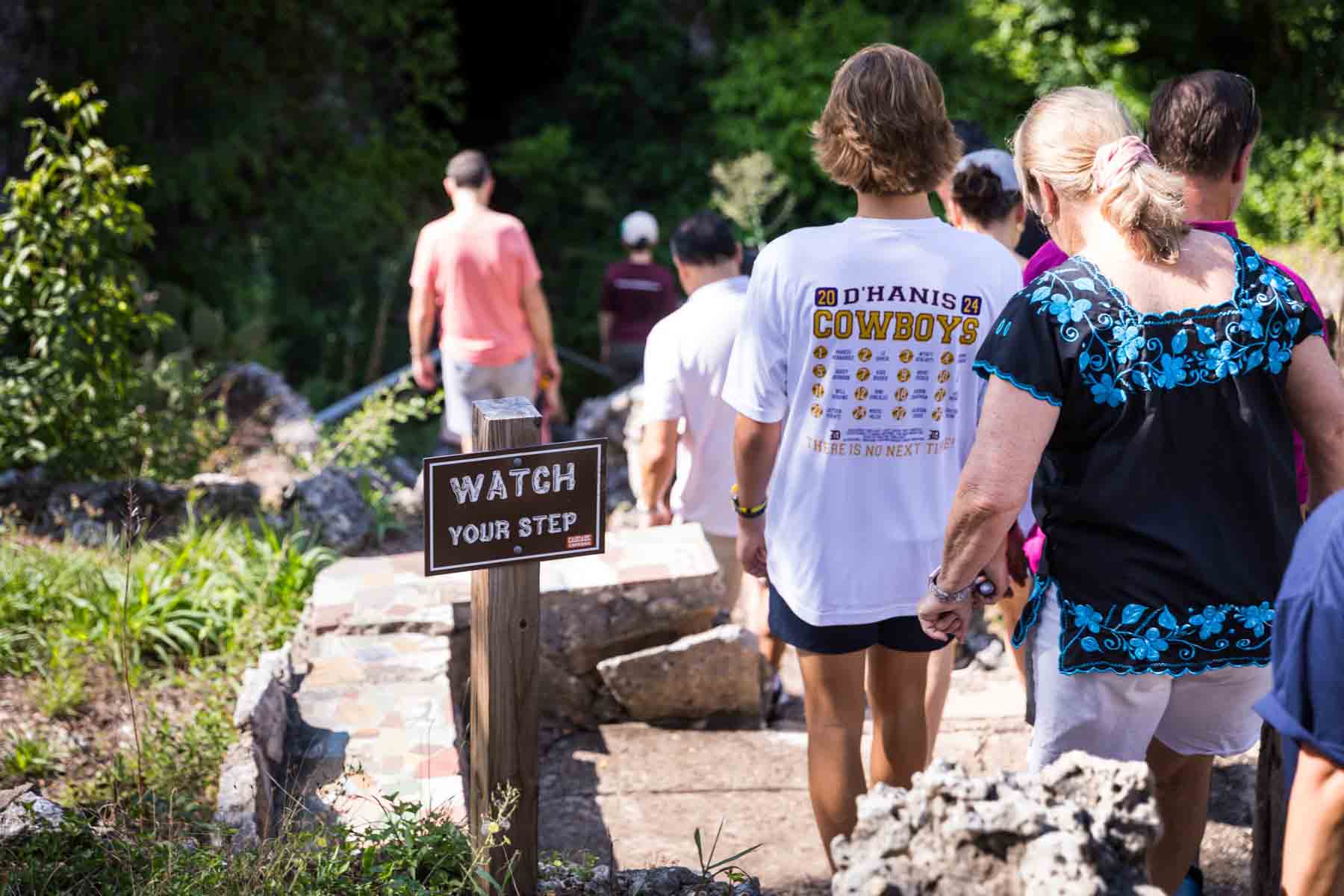 Visitors walking past 'Watch Your Step' sign in Cascade Caverns for an article entitled, ‘Visiting Boerne, Texas: Everything You Need to Know’