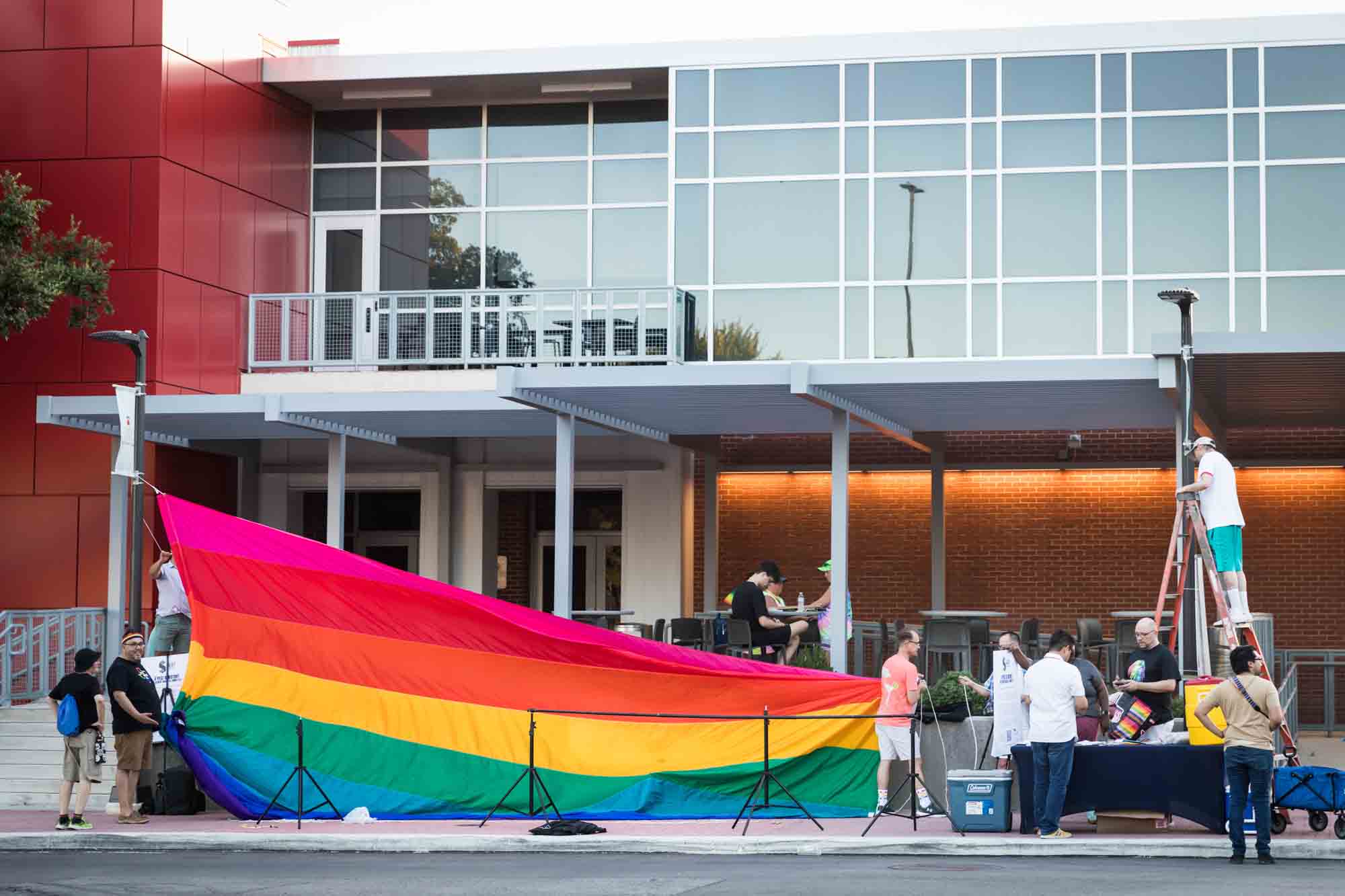 San Antonio gay pride parade photos of several people attempting to display very large rainbow flag in front of building