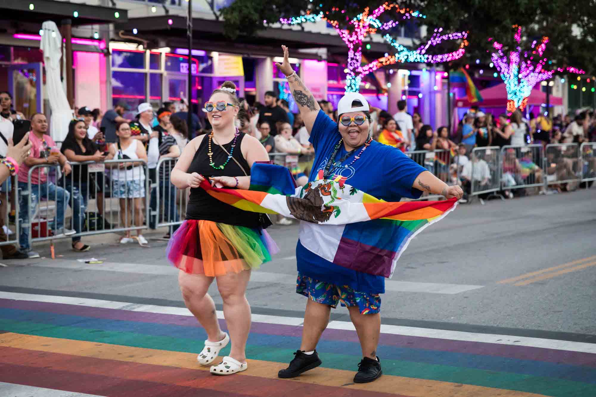 San Antonio gay pride parade photos of two people enthusiastically waving the rainbow flag in the street