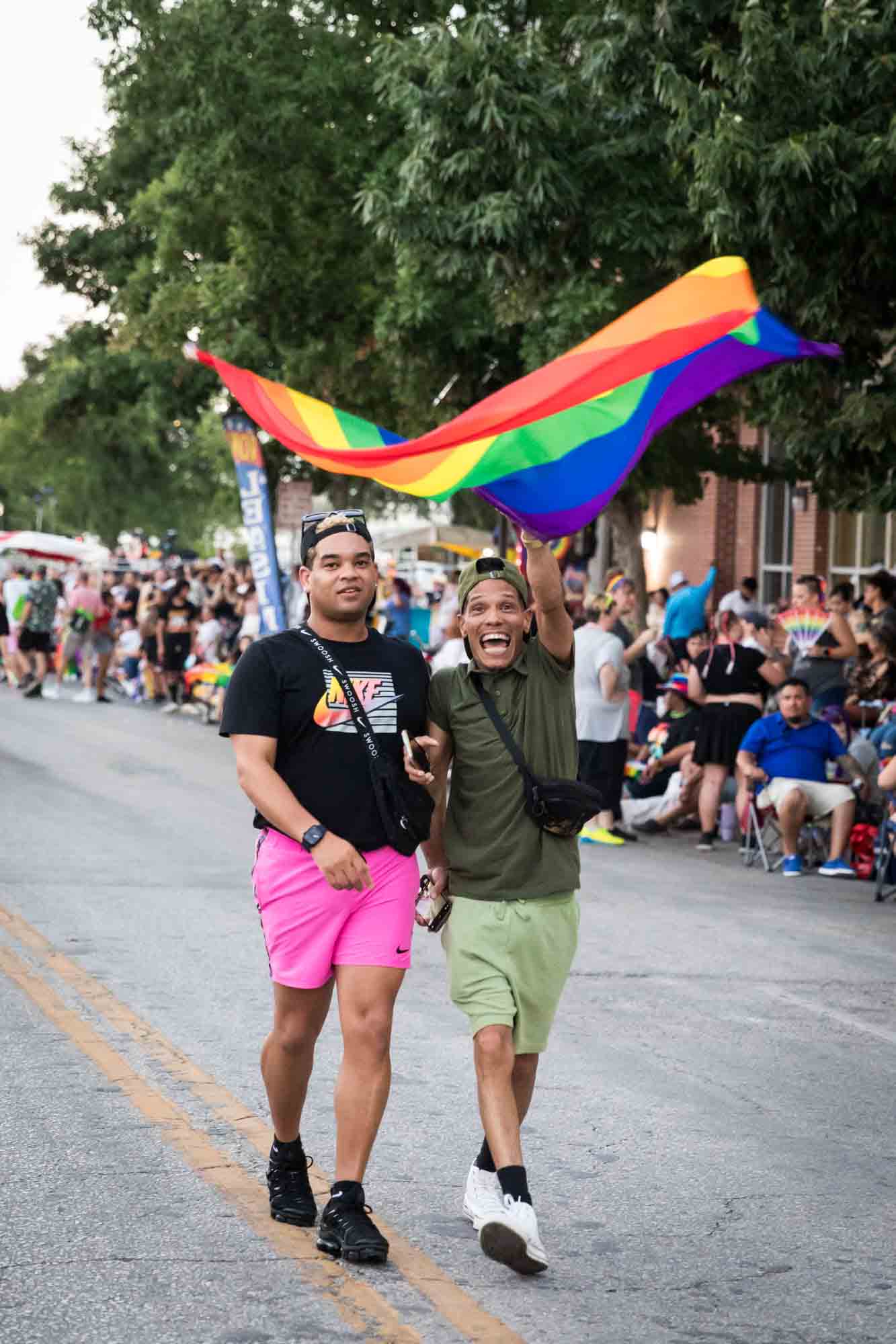 San Antonio gay pride parade photos of two people enthusiastically waving the rainbow flag in the street