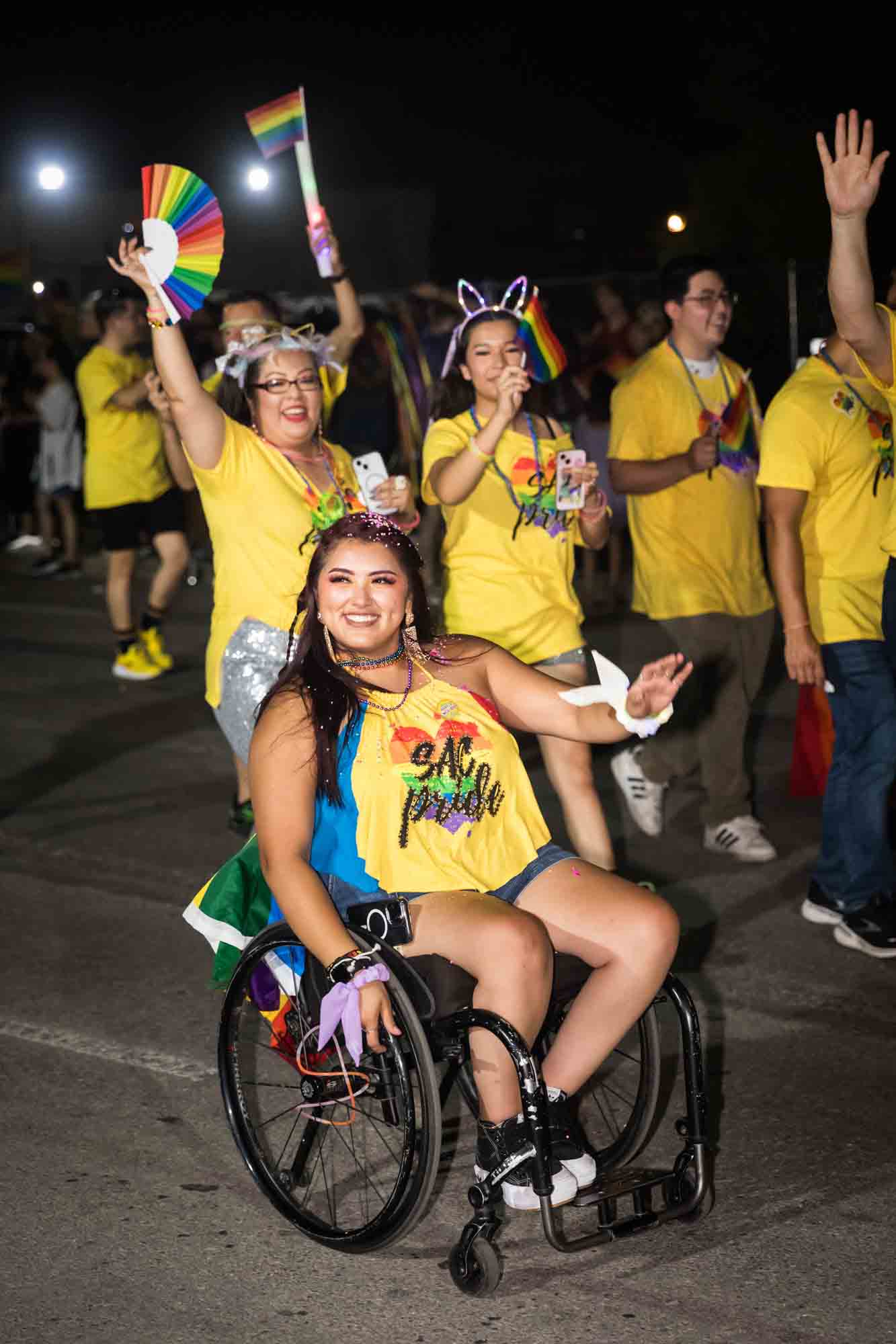 San Antonio gay pride parade photos of woman in wheelchair and other people in yellow shirts walking in parade